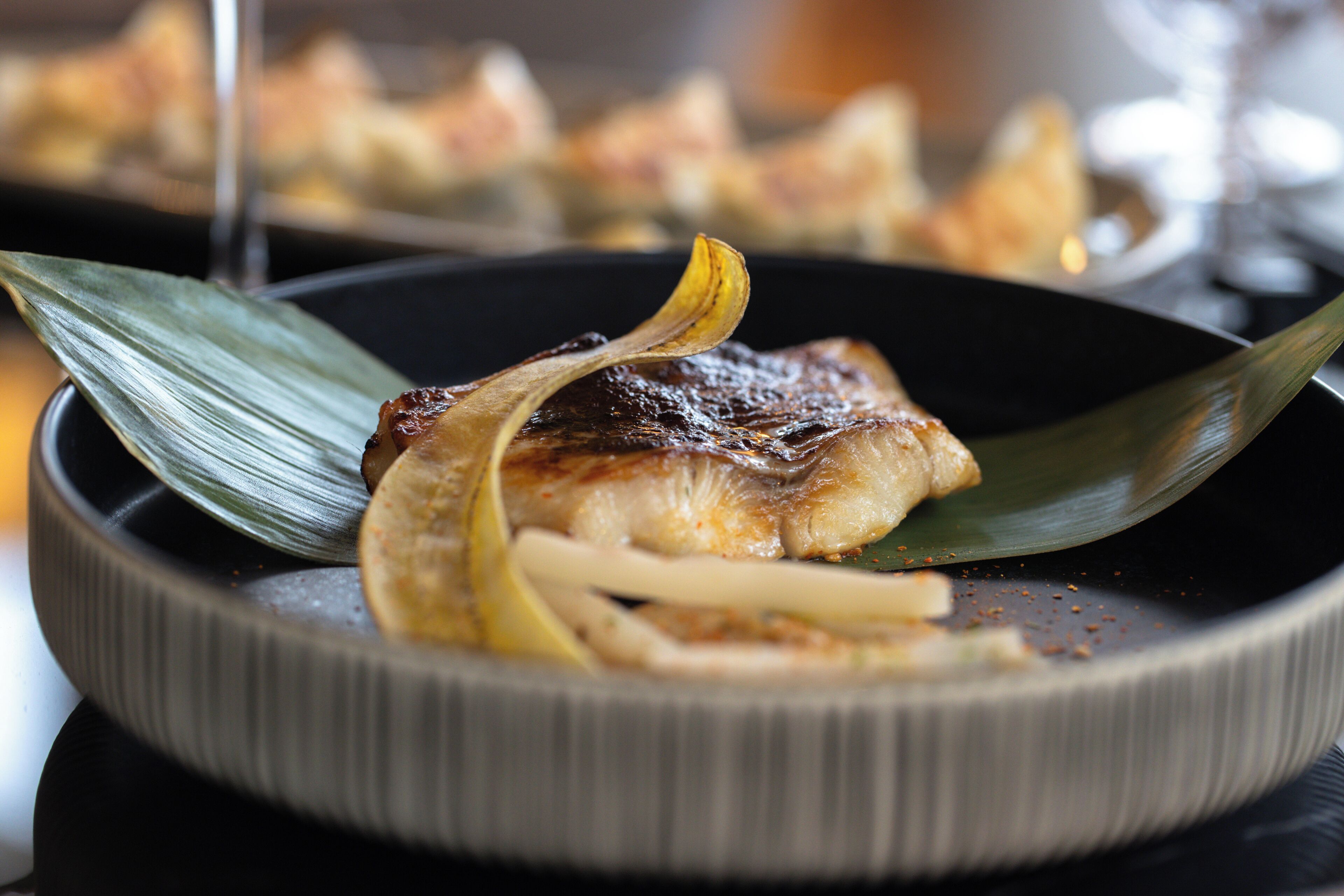 A plate with a grilled meat, garnished with a leaf and a slice of lemon.