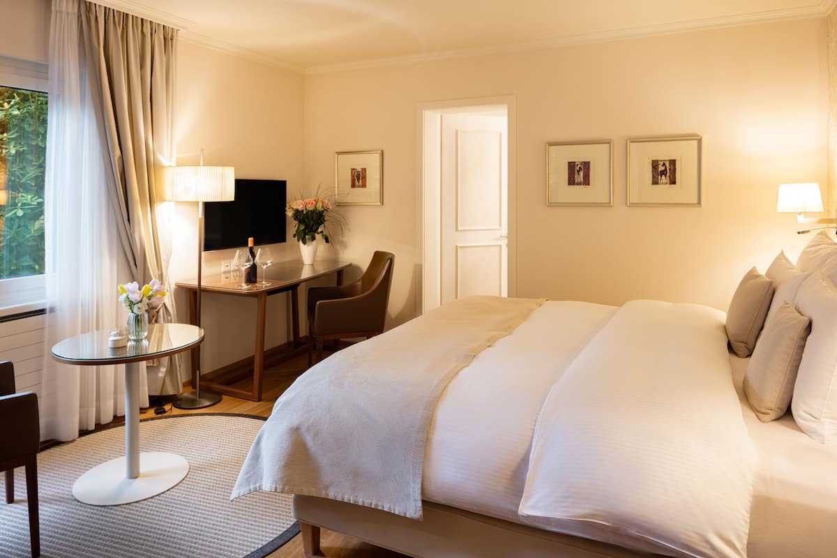Een hotelkamer met een groot bed, een bureau met stoel, een tafeltje met bloevasen en een televisie aan de muur.