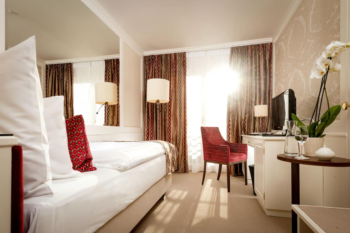 Een hotelkamer met een bed, een bureau, een stoel, een televisie en een potplant.