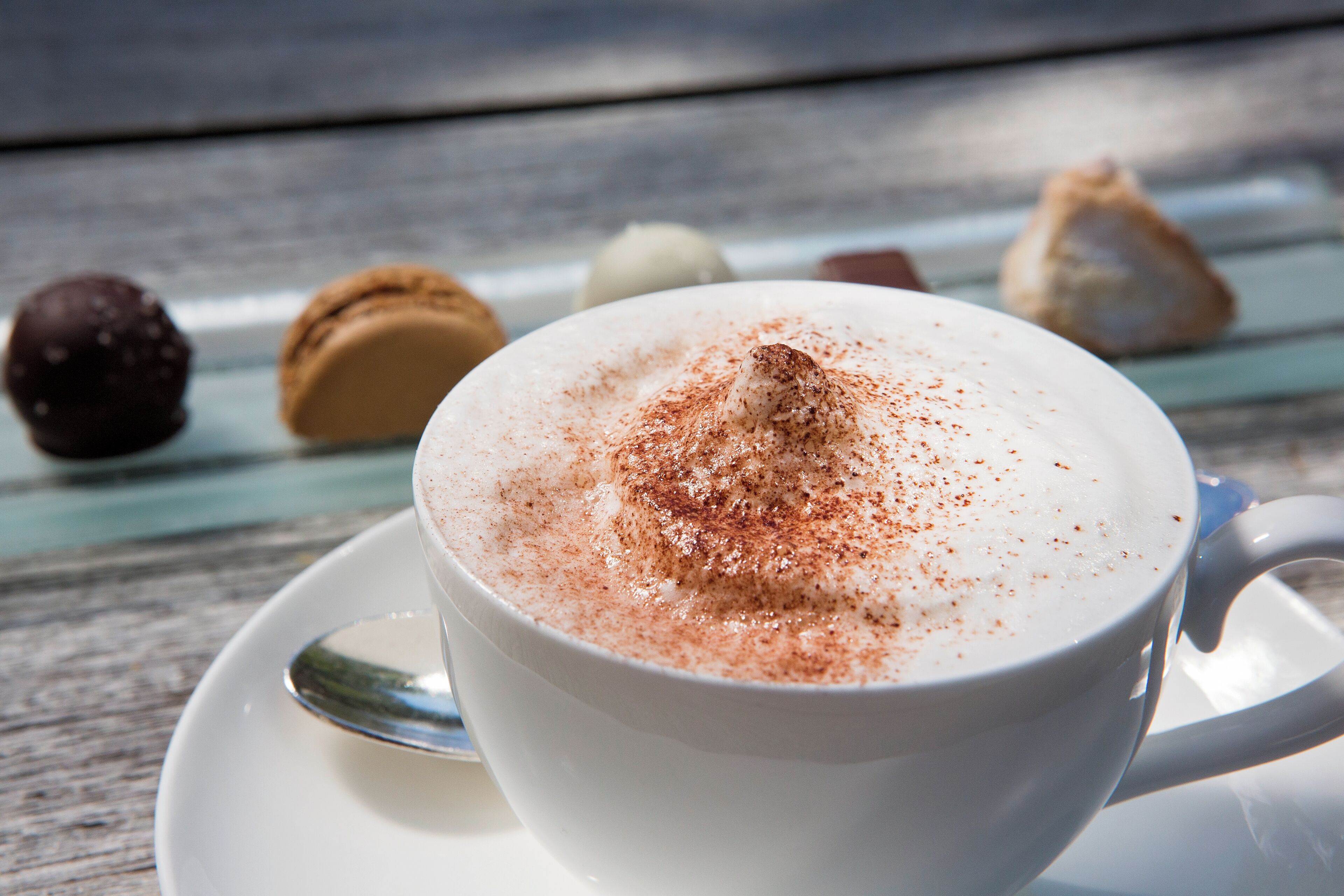 Una tassa de cafè blanc amb una mica de canyella sobre un calderó, damunt d'un taulell de fusta.
