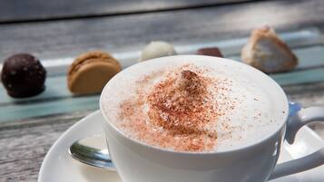 Una tassa de cafè blanc amb una mica de canyella sobre un calderó, damunt d'un taulell de fusta.