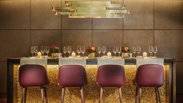 Zona de bar con diseño moderno, que incluye una mesa larga con varias sillas, una lámpara decorativa encima y una pared con textura.