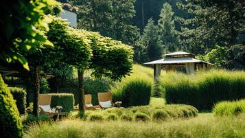 A serene garden with a gazebo, neatly trimmed hedges, and wicker furniture.