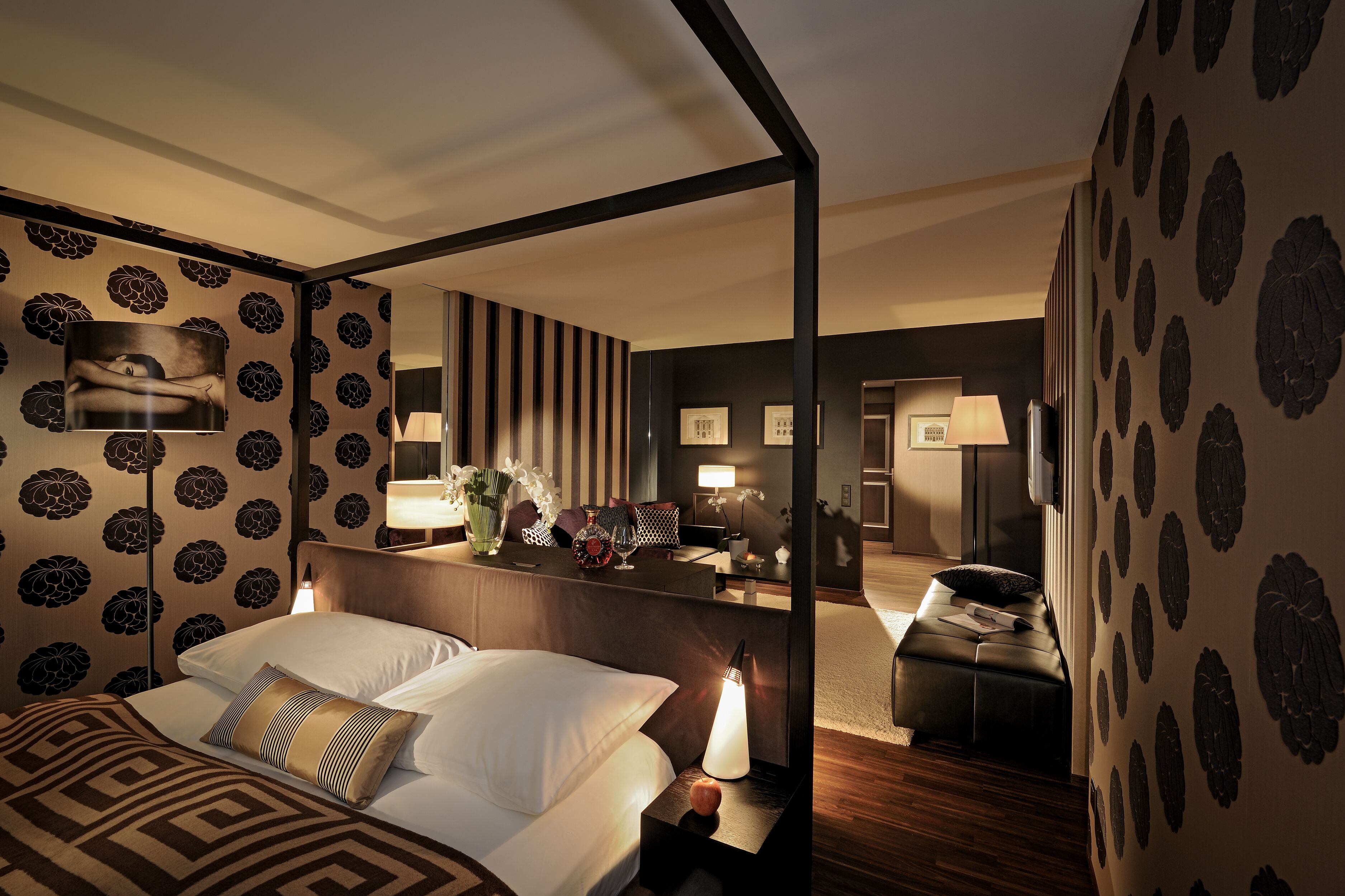 A hotel room with a bed, bedside table, lamp, and a mirror reflecting the room.