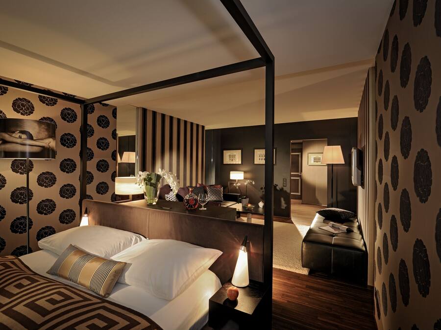A hotel room with a bed, bedside table, lamp, and a mirror reflecting the room.