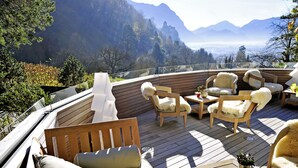 Een terras met houten meubilair en uitzicht op bergen.