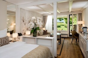 A hotel room with a large bed, a sitting area with a view, a desk with a lamp, and a bathroom visible through an open door.