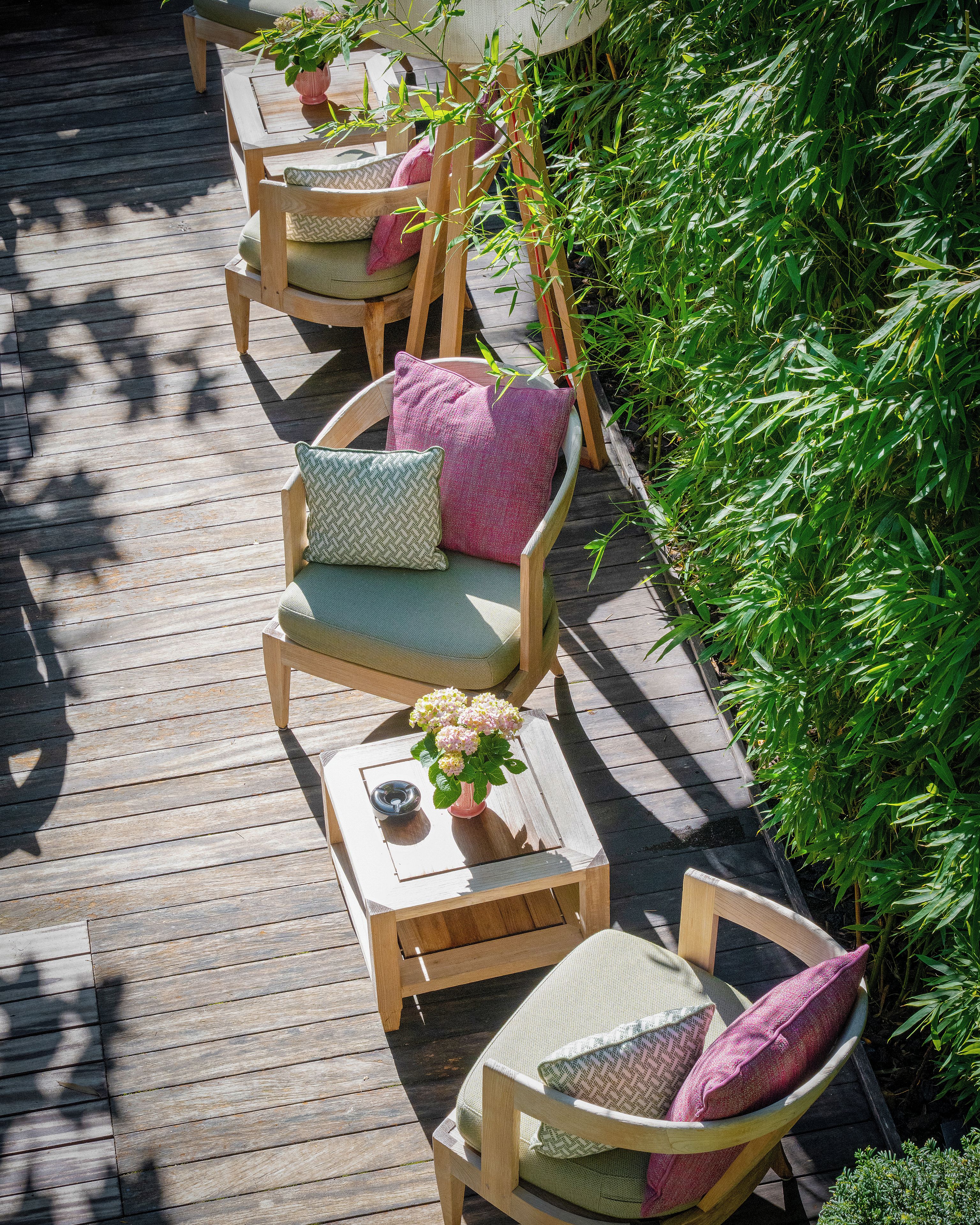 A wooden deck with outdoor furniture, including chairs and a table, surrounded by greenery.