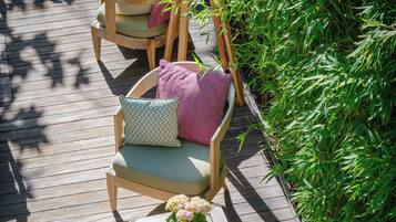A wooden deck with outdoor furniture, including chairs and a table, surrounded by greenery.