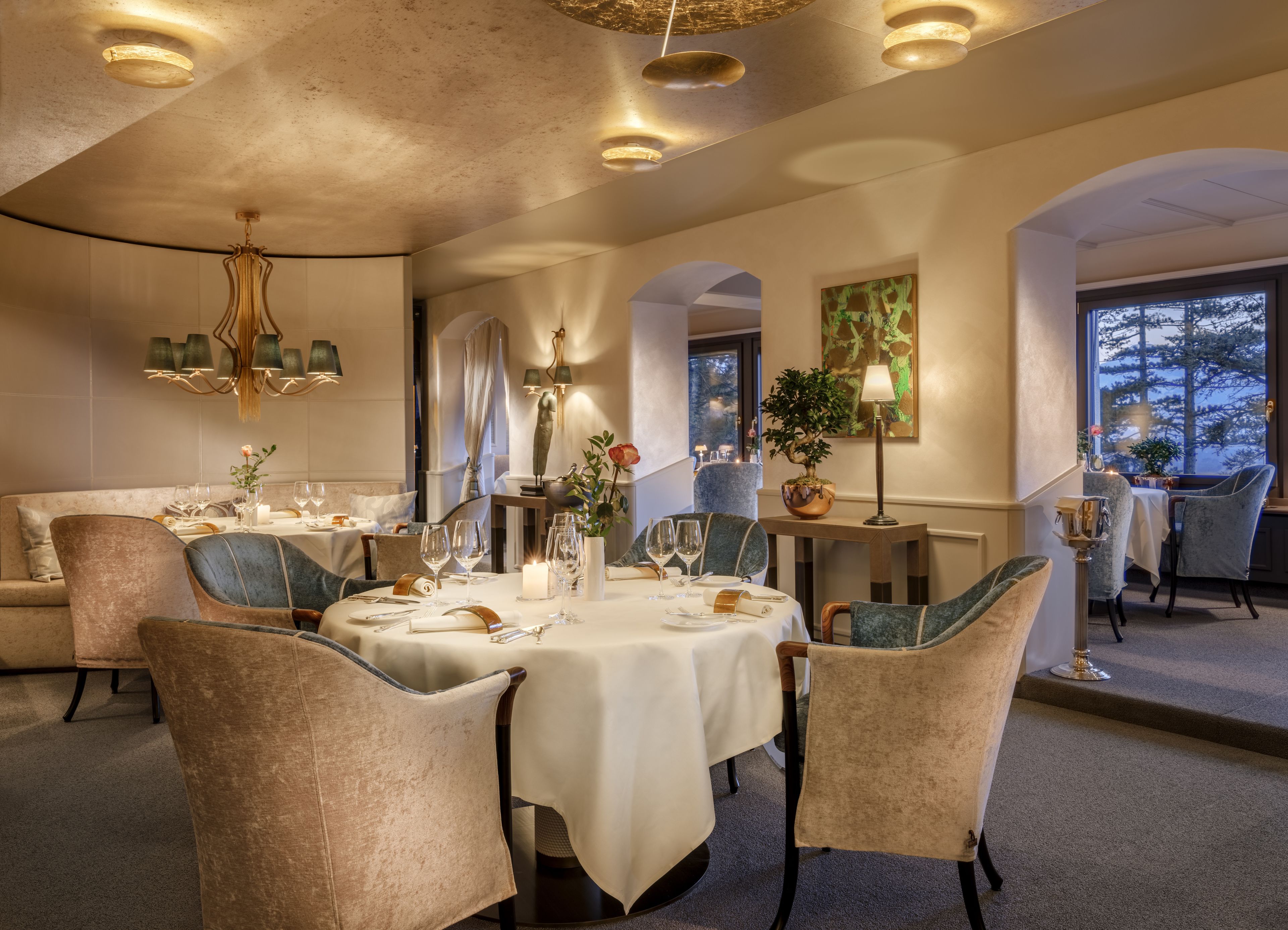 A dining area with round tables, cushioned chairs, and a chandelier.