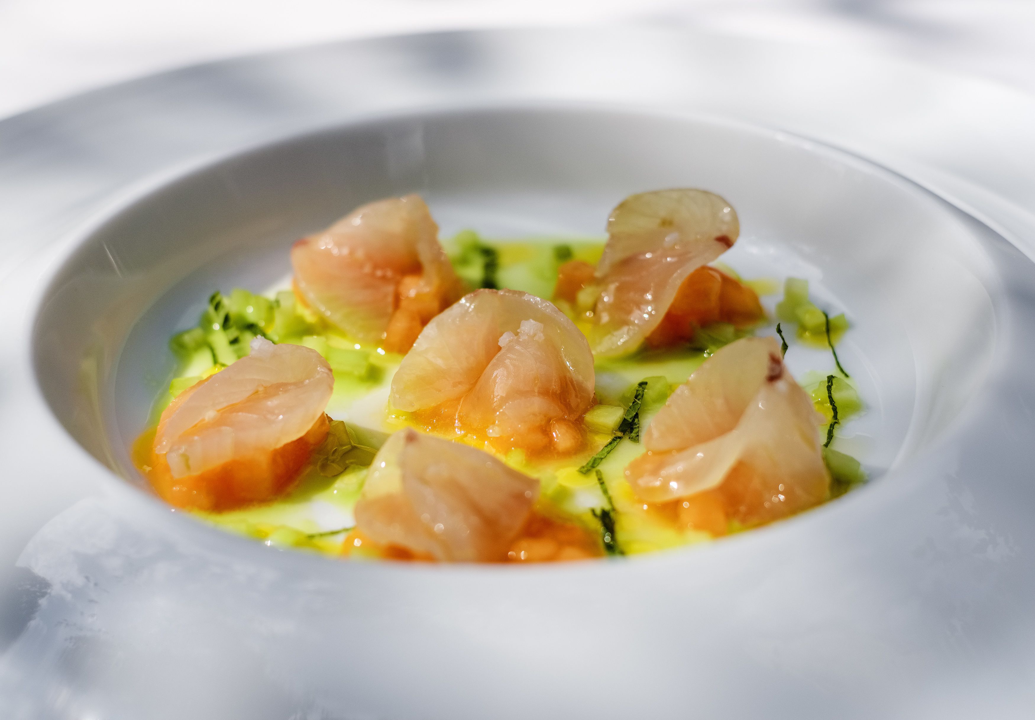 Un plato blanco con un guiso de mariscos, posiblemente salmón, adornado con hierbas y una salsa amarilla.