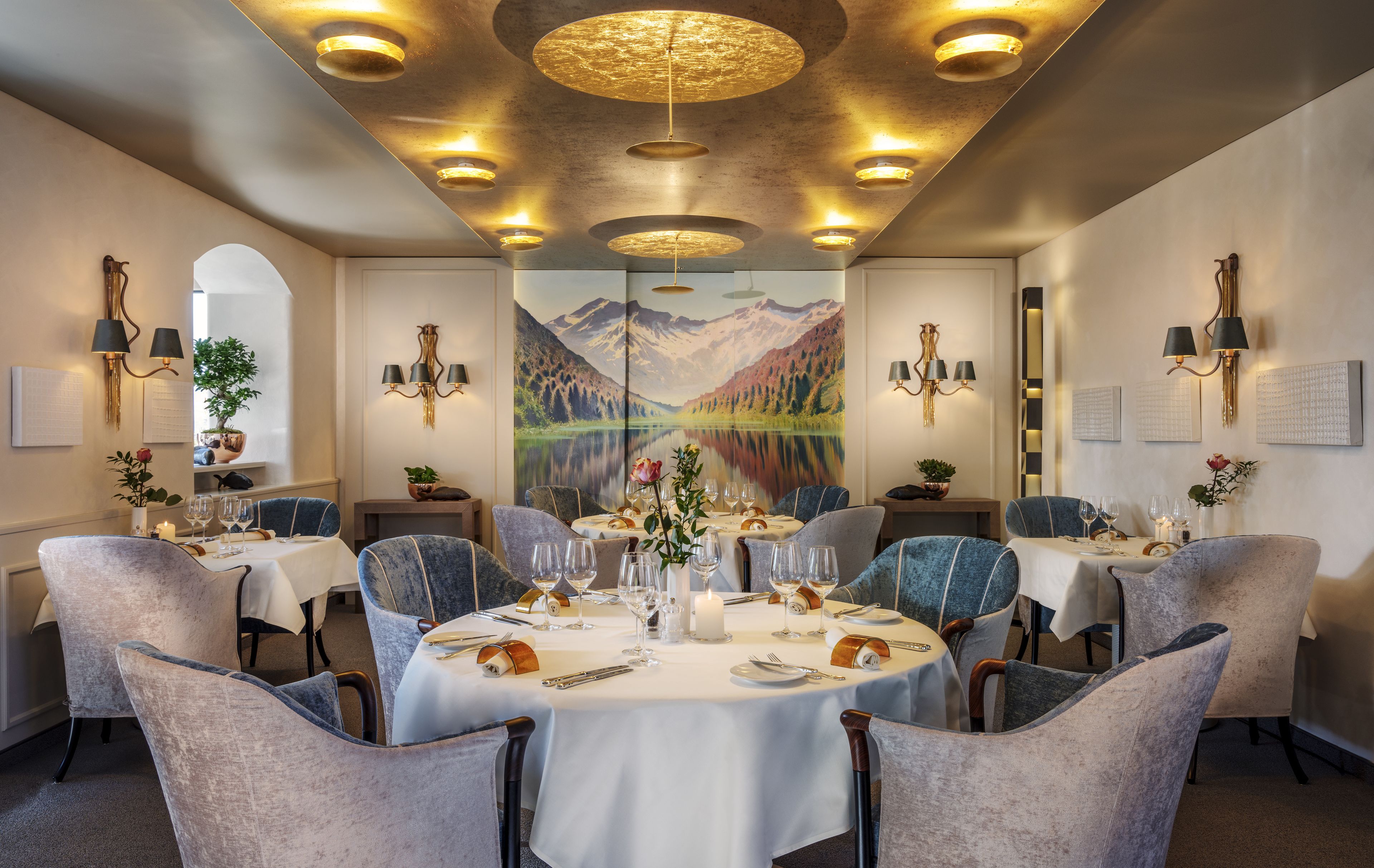 Un comedor con mesas redondas, sillas y un mural de un paisaje montañoso.