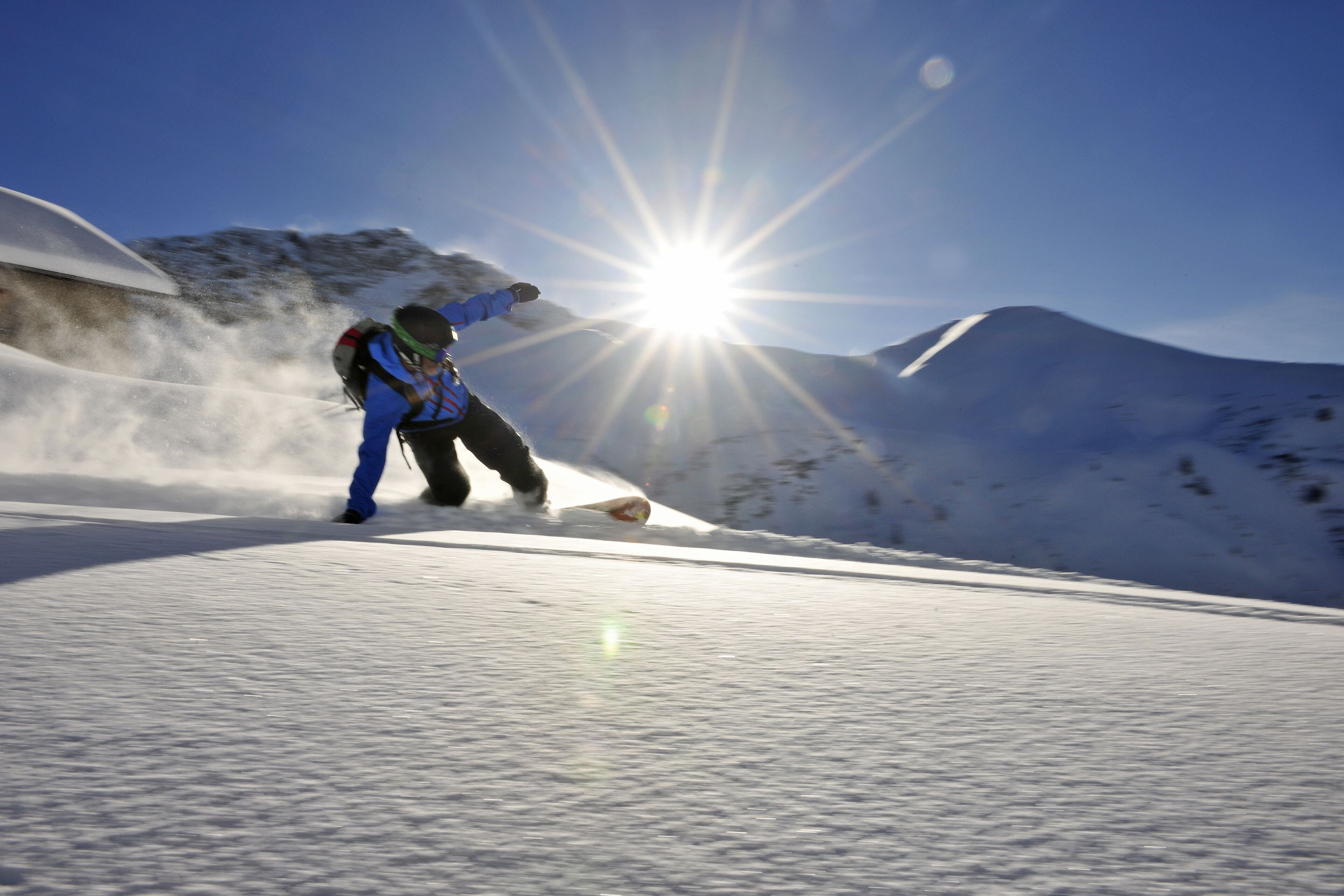 A snowboarder on a snowy slope with a clear sky and sun shining.