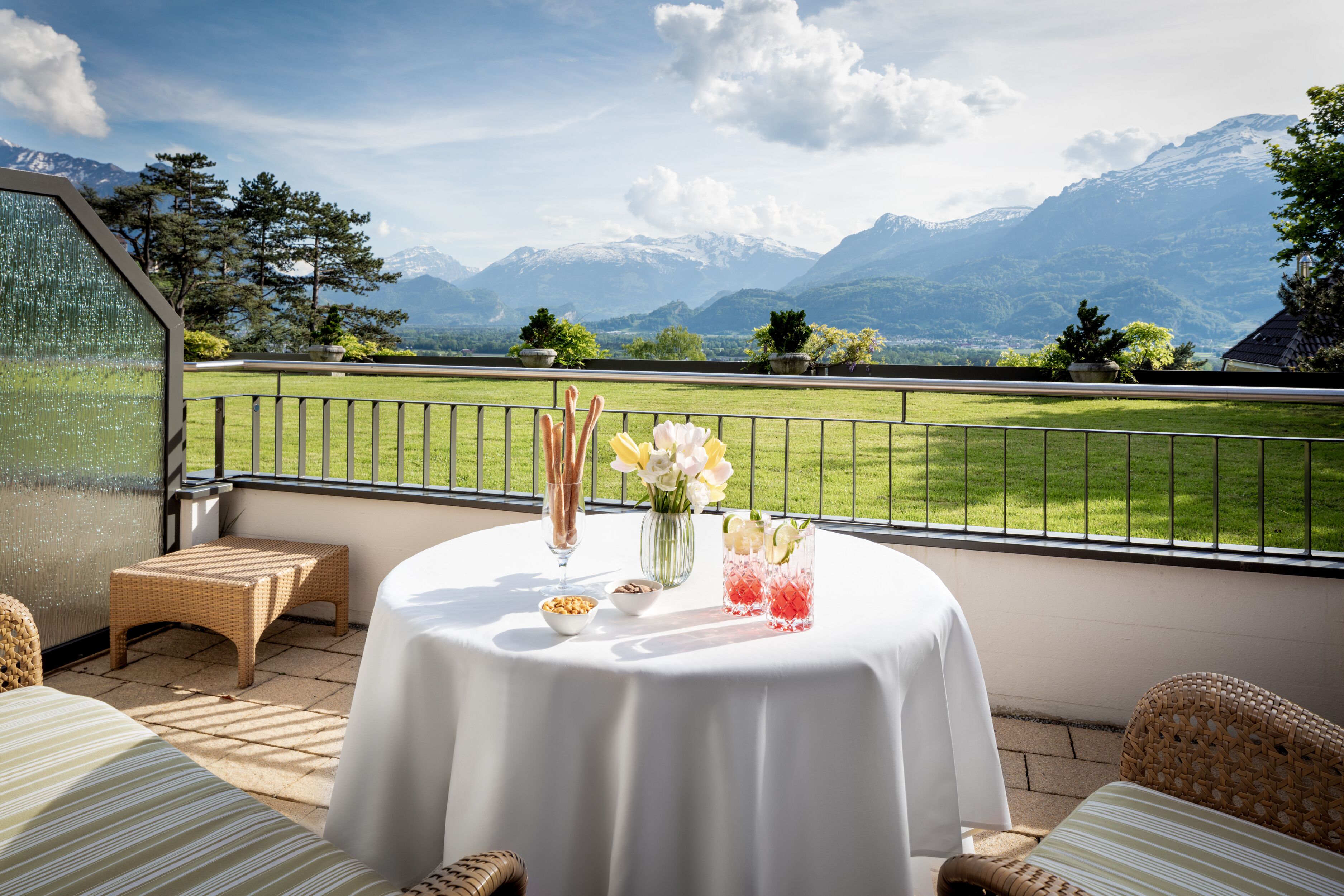 A terrace with a table set for two, overlooking a mountain landscape.