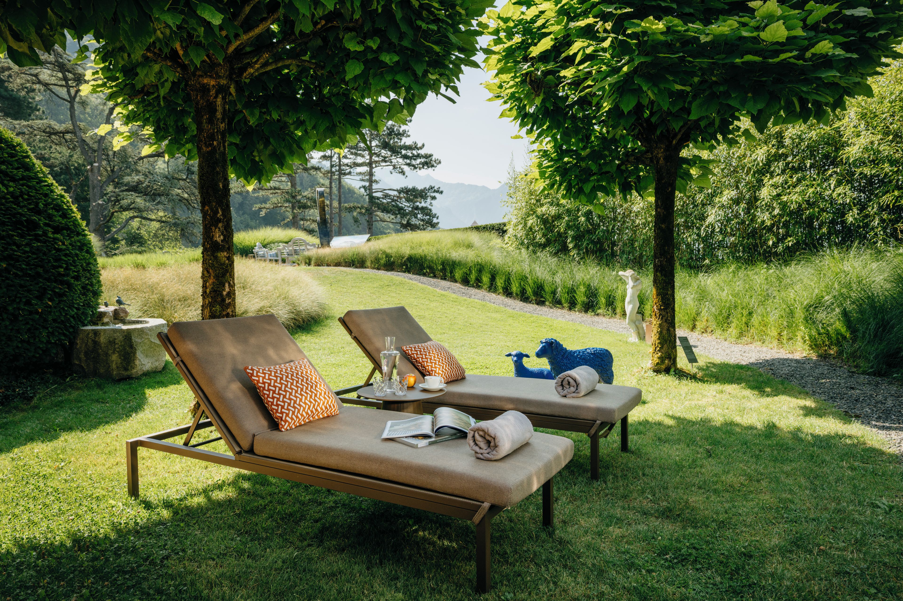 Twee loungestoelen met handdoeken en een glas water, gelegen in een gazon met bomen en uitzicht op de heuvels.