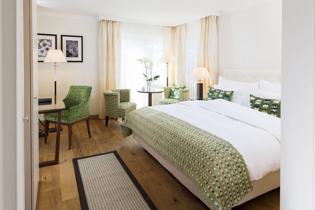 Een hotelkamer met een groot bed, twee fauteuils, een kleine tafel en een lamp.