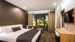 Een hotelkamer met een groot bed, een bureau, een stoel, een televisie en uitzicht op de stad.