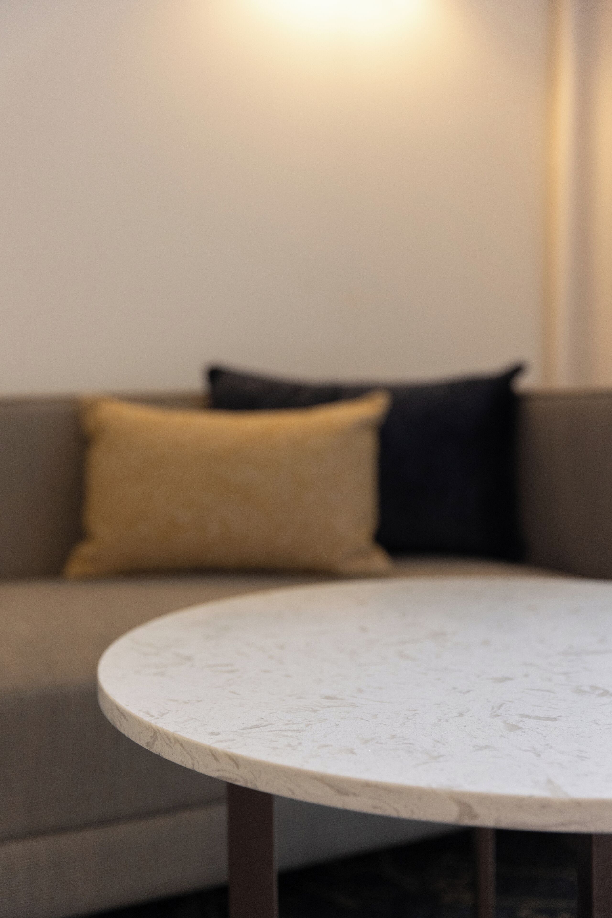 A round table with a marble top, positioned in front of a sofa with two cushions.