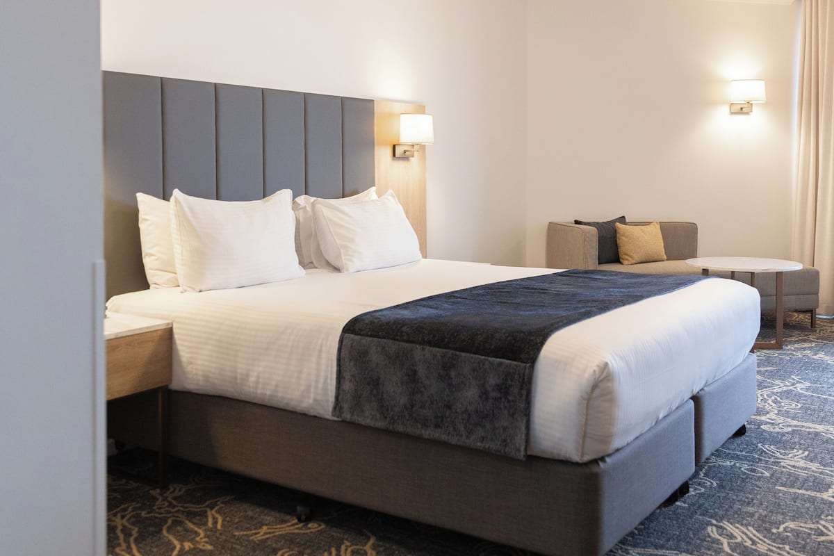 Een hotelkamer met een groot bed, een nachtkastje, een klein tafeltje en een bank.