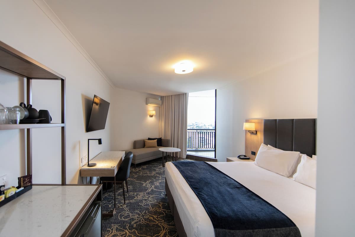 Een hotelkamer met een bed, een bureau, een stoel, een televisie, een raam met uitzicht en een balkon.