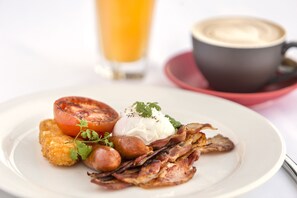 Enjoy a hearty breakfast with a poached egg, crispy bacon, grilled tomato, and fried potato, accompanied by a glass of orange juice and a cup of coffee.