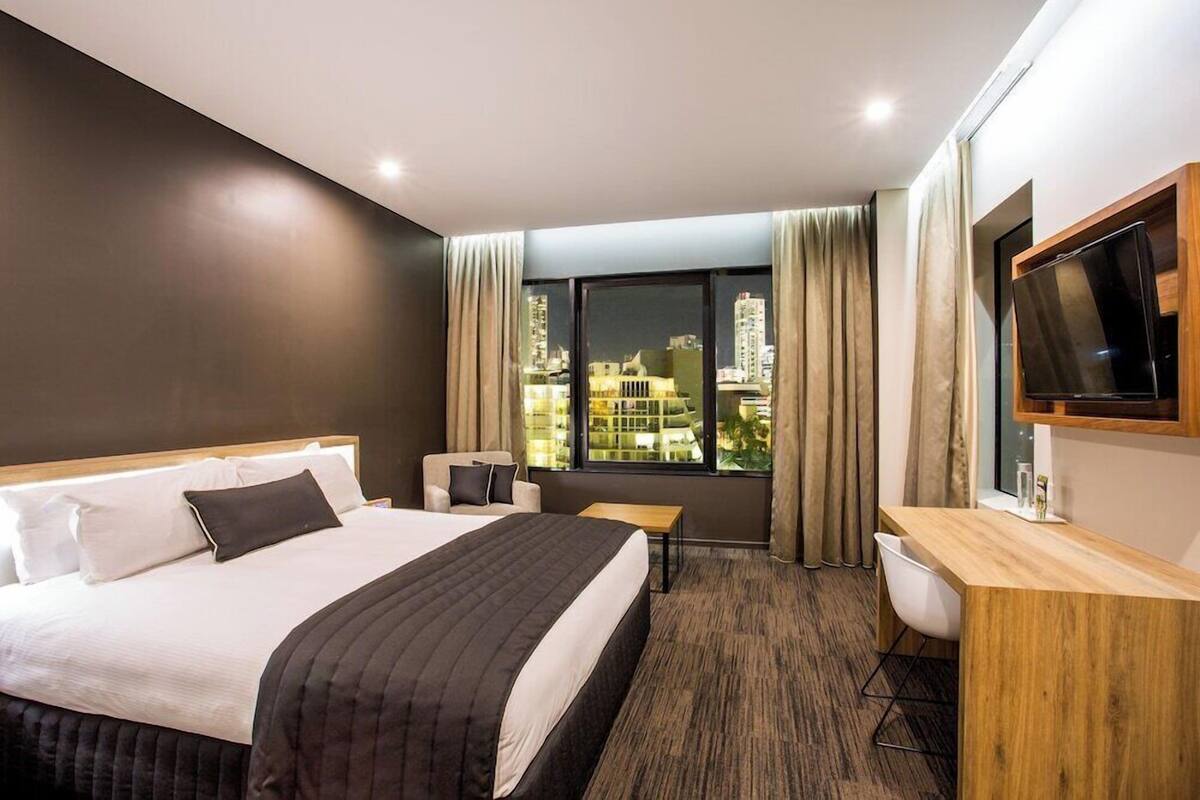 Hotelkamer met een groot bed, een bureau, een stoel, een televisie en een raam met uitzicht over de stad.