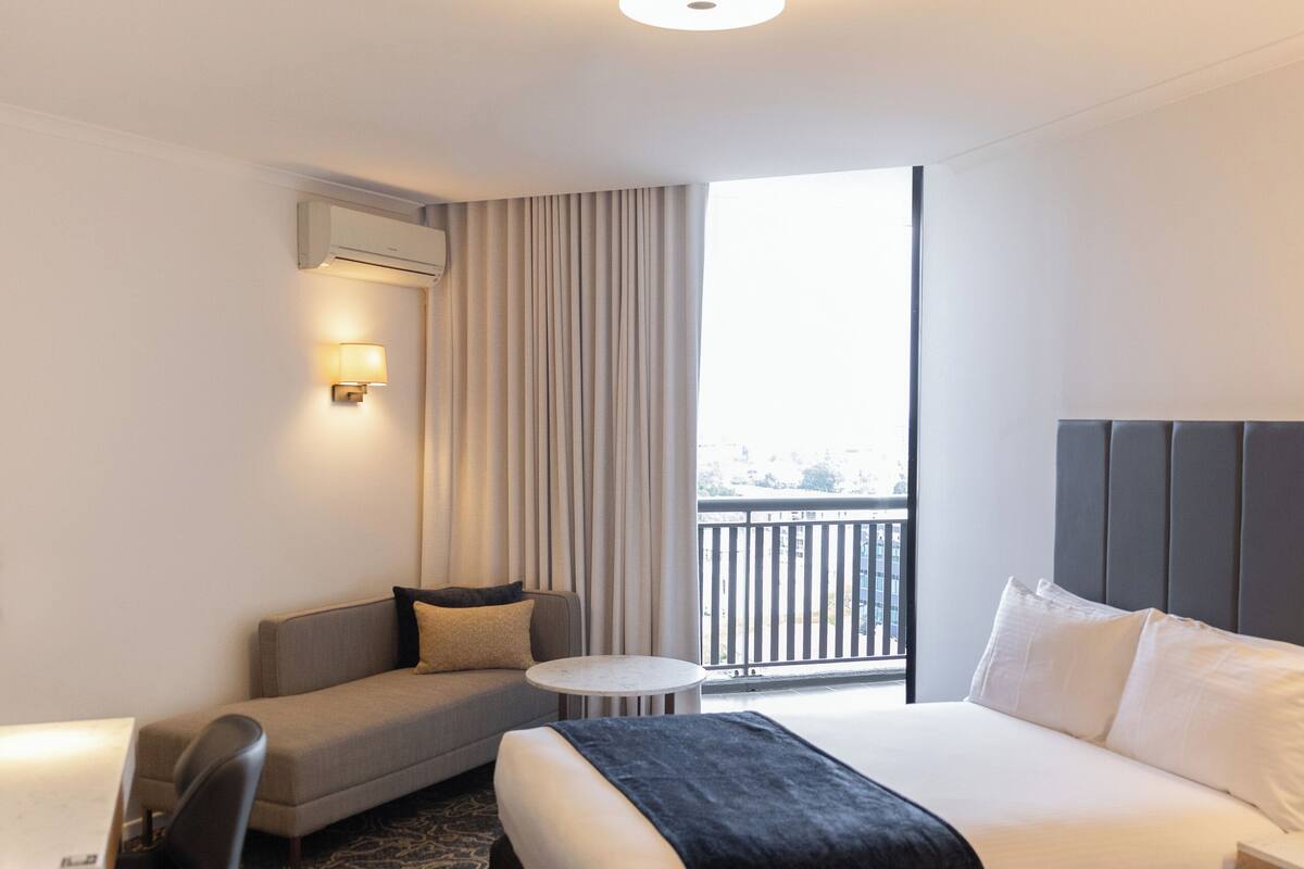 Een hotelkamer met een bed, een bank, een bureau en een balkon met uitzicht.