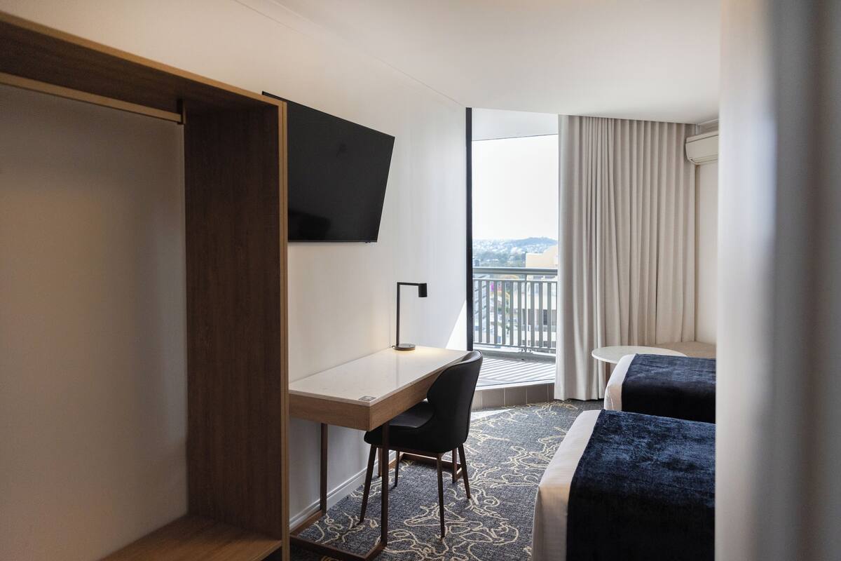 Een hotelkamer met een bureau, een stoel, een bed en een televisie aan de muur.
