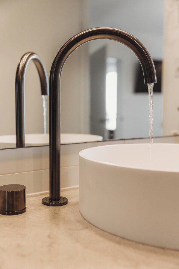 Un baño moderno con un lavamanos redondo blanco, un grifo negro elegante y un pequeño recipiente metálico.