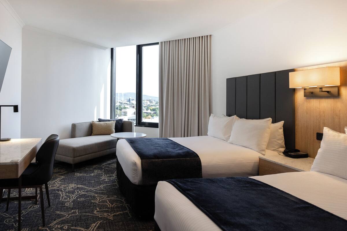 Een hotelkamer met een groot bed, een bank, een bureau en uitzicht over de stad.