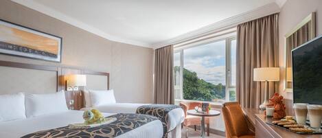 Une chambre d’hôtel avec deux lits, une table à manger, une chaise, un téléviseur et un balcon offrant une vue panoramique.