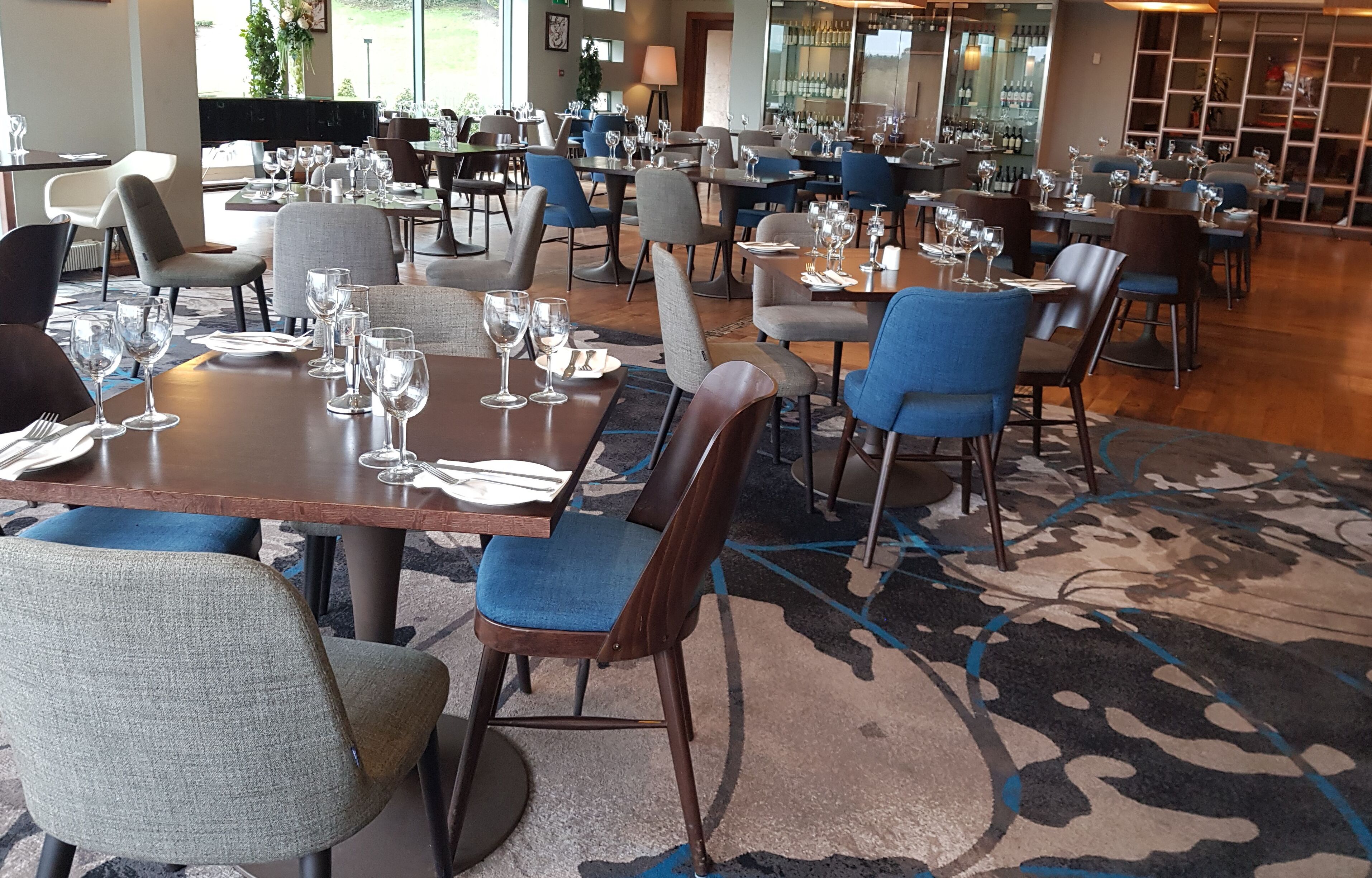 A restaurant with multiple tables and chairs, some with wine glasses and cutlery.