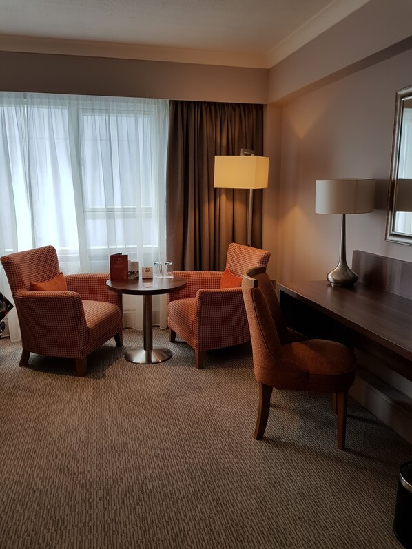A hotel room with a checkered armchair, a round table, a lamp, and a bed.