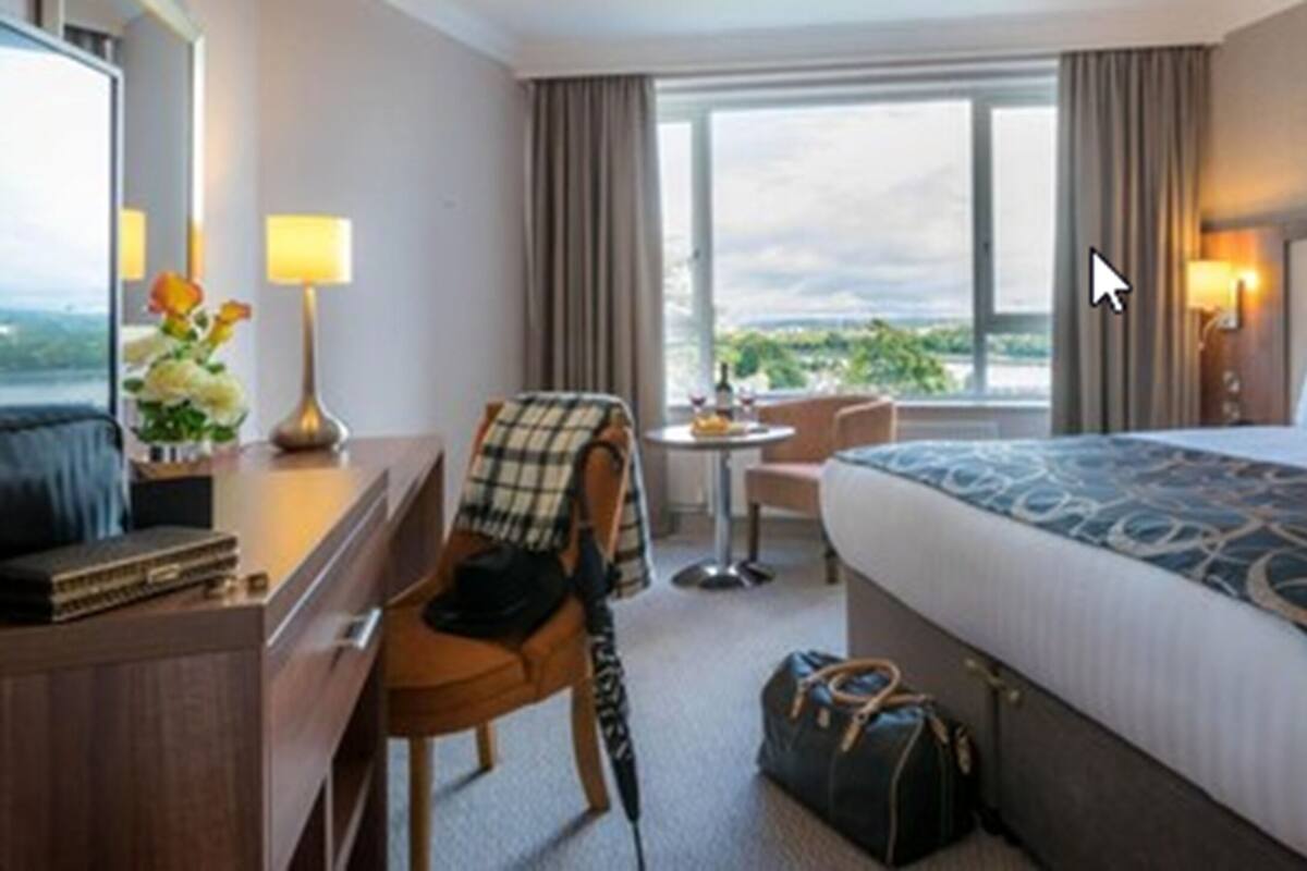 Habitación de hotel con cama, escritorio, silla, una mesita y ventana con vistas.
