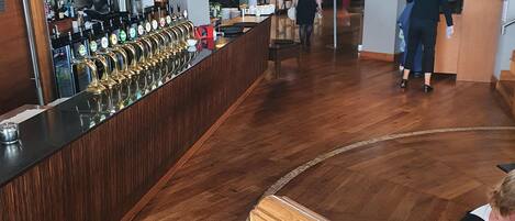A bar area with a long counter, multiple taps, and a wooden floor.