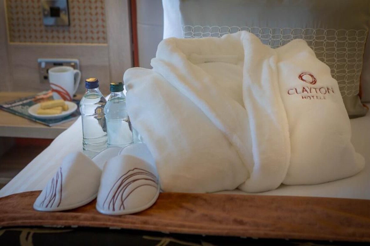 Habitación de hotel con una cama bien hecha, un tray con artículos de tocador y un plato de desayuno sobre la mesita de noche.