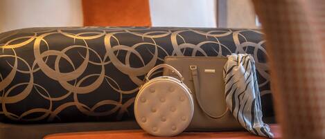 A bed with a patterned headboard, a round white pillow, and a beige handbag on a red ottoman.