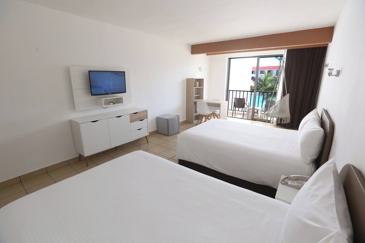 Une chambre d’hôtel avec deux lits, une télévision, un bureau et un balcon donnant sur la piscine.