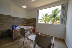 A modern bathroom with a bathtub, two chairs, a vanity with a mirror, and a window with a view of palm trees.