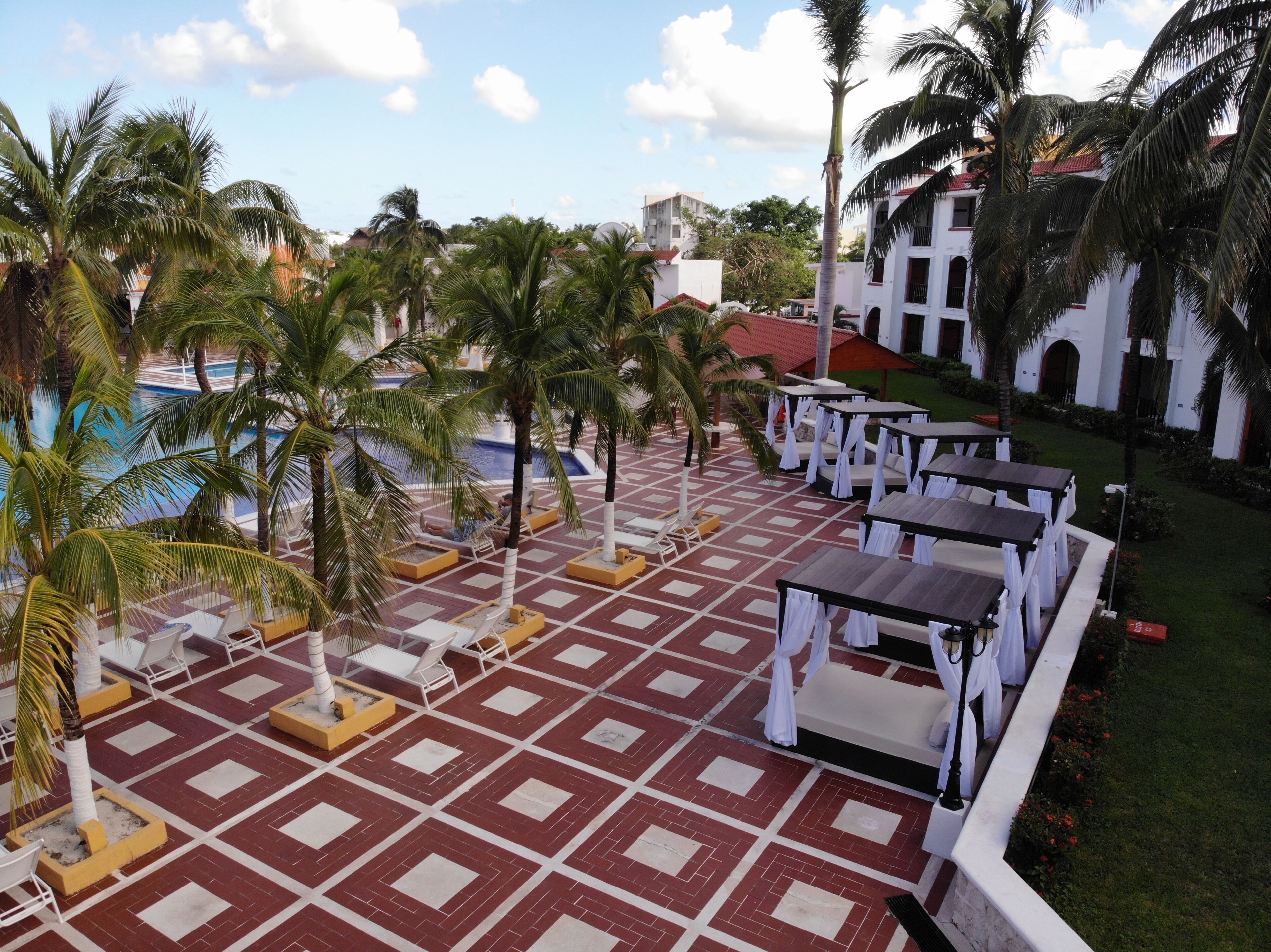 Zona junto a la piscina con palmeras, mobiliario exterior y suelo estampado.