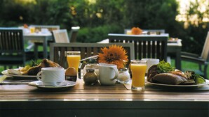 A breakfast table set outdoors with plates of food, cups, and a glass of orange juice.