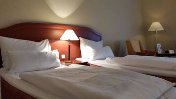 Una habitación de hotel con dos camas, una mesita de noche con una lámpara, una silla y una mesita de noche con un marco de foto.