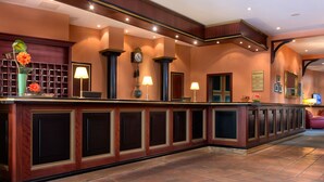 A reception area with a long counter, multiple lamps, a clock, and a wall-mounted display.