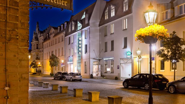 A hotel with a sign reading "Ratskeller" and "SORAT HOTEL BRUNNENHAUSEN" with a cobblestone street and parked cars.