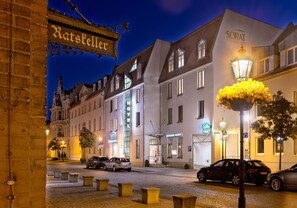 A hotel with a sign reading "Ratskeller" and "SORAT HOTEL BRUNNENHAUSEN" with a cobblestone street and parked cars.