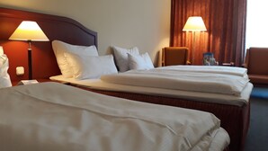 A hotel room with two beds, each with white linens, a wooden headboard, and two bedside lamps.