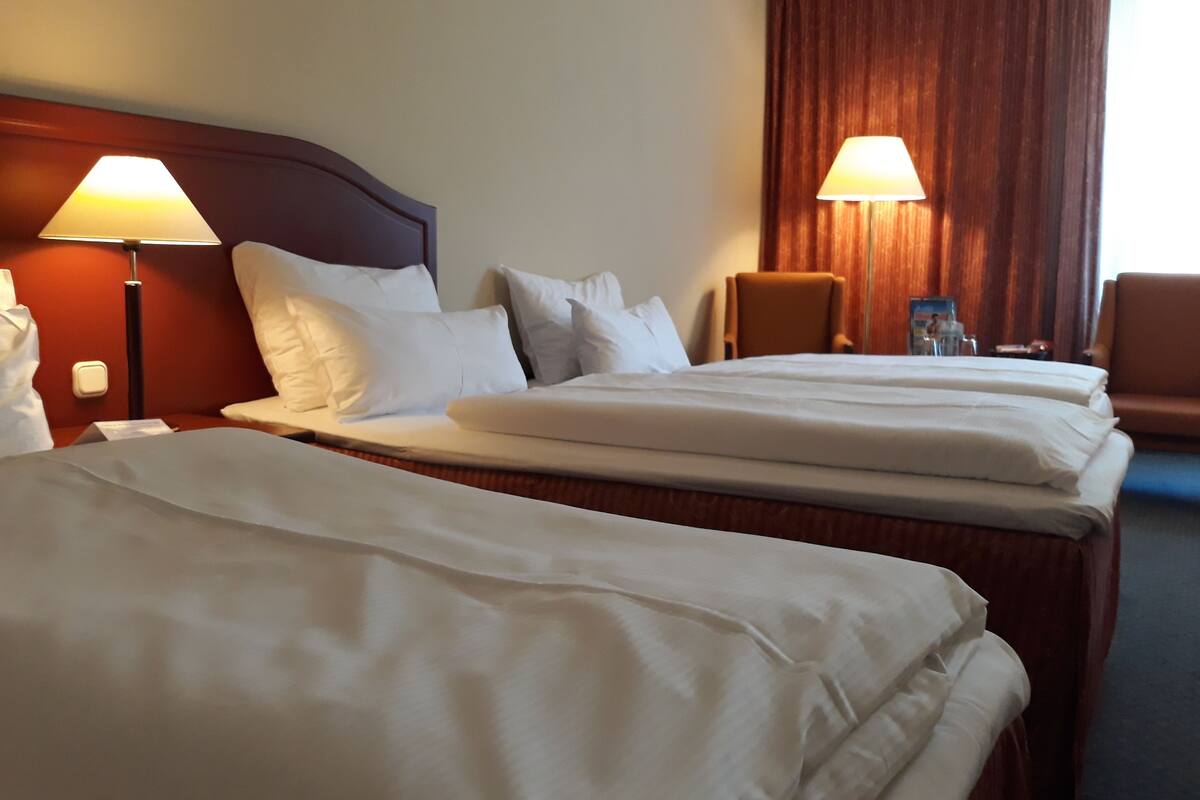 Une chambre d’hôtel avec deux lits, chacun doté de draps blancs, d’une tête de lit en bois et de deux lampes de chevet.