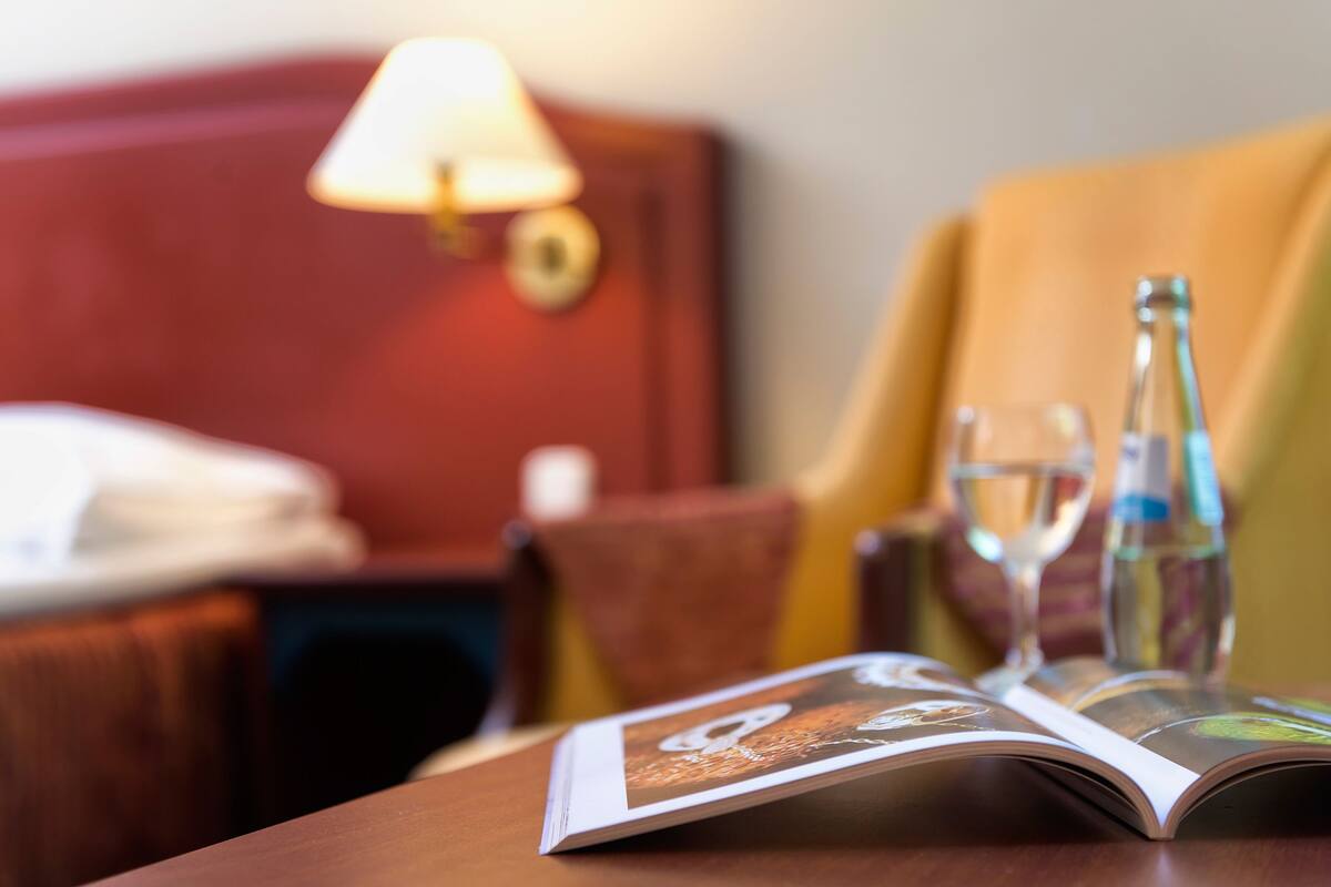 Une chambre d’hôtel avec un lit, une table de chevet, une lampe, une bouteille et un verre d’eau sur une table.