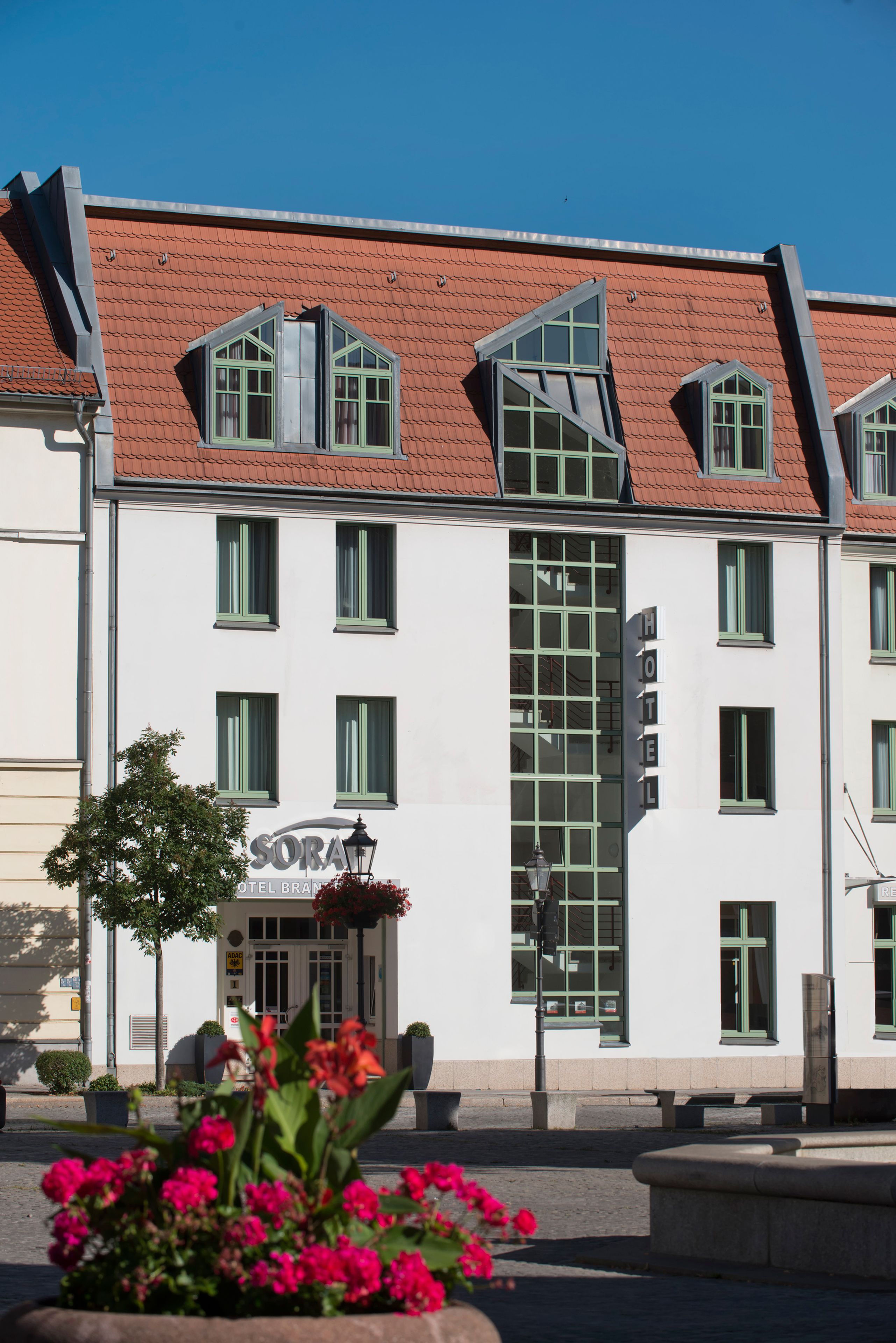 A hotel with a white facade, green window frames, and a red roof.