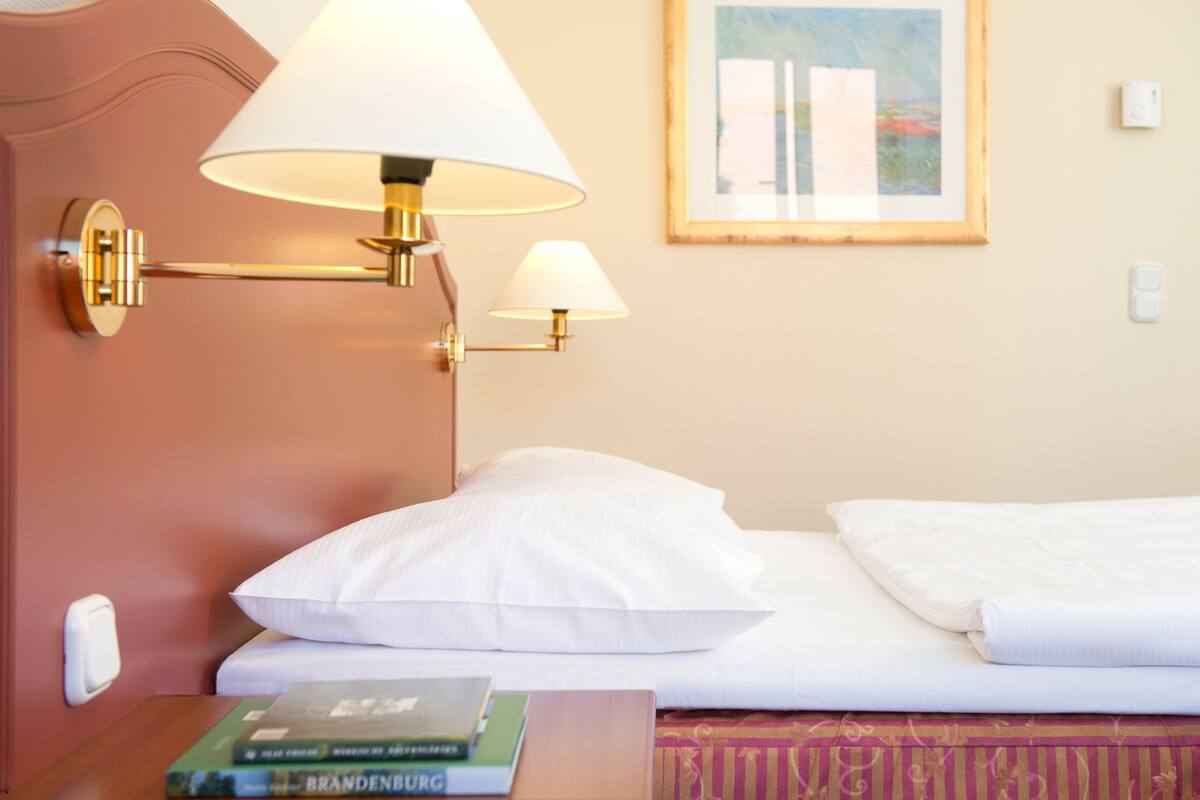 Une chambre d’hôtel avec un lit, deux lampes fixées au mur, un tableau encadré accroché au mur et un livre sur la table de chevet.